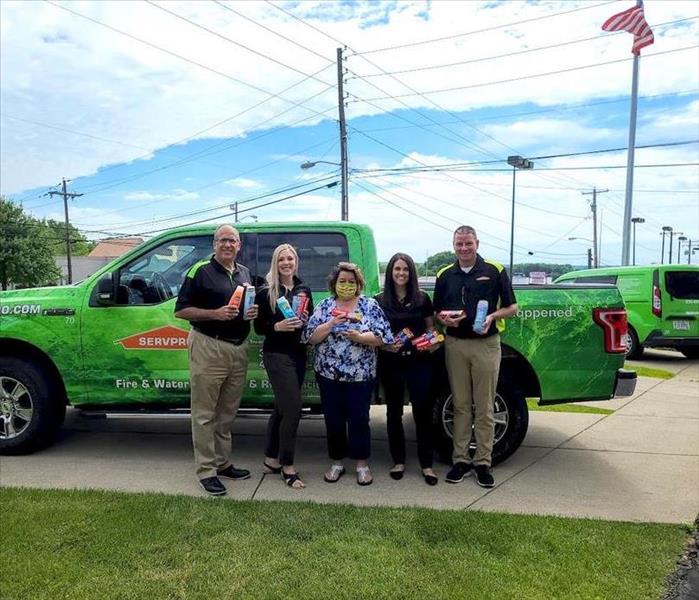 image of 4 SERVPRO workers along with business partner holding donated goods smiling in-front of servpro truck