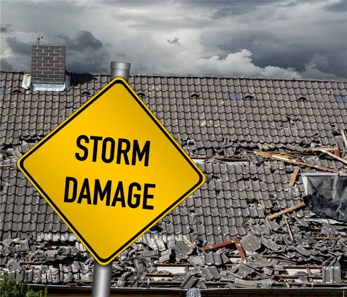 A yellow street sign read "Storm Damage" and sits in front of a damaged roof.