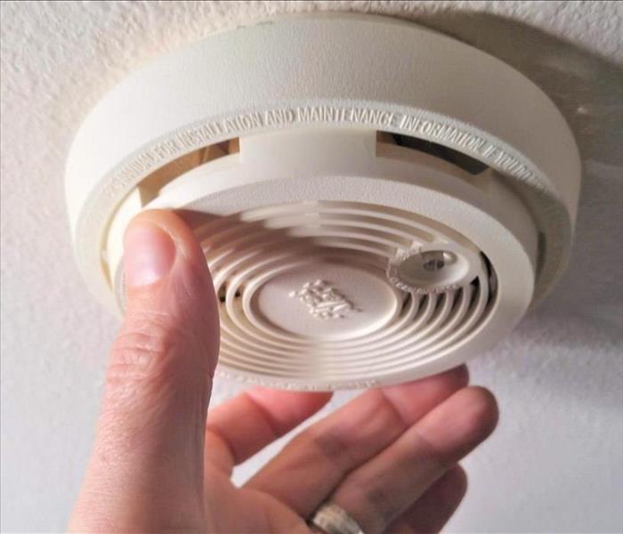 image of hand testing a smoke alarm but taking it off and back on