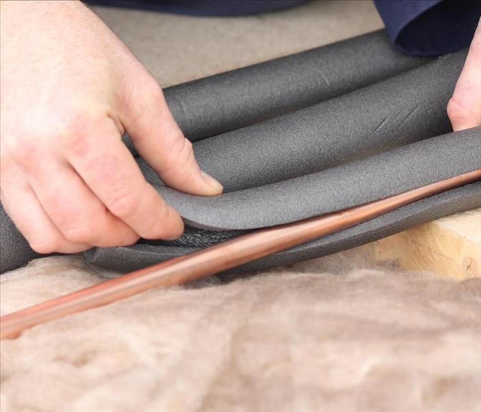 image of person wrapping insulation around copper pipes