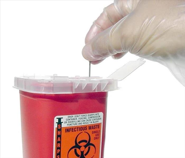  hand placing a needle into a red bio safety disposal container