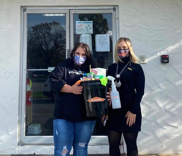 image of servpro employee with local school teacher smiling for a picture while holding a bucket of cleaning supplies